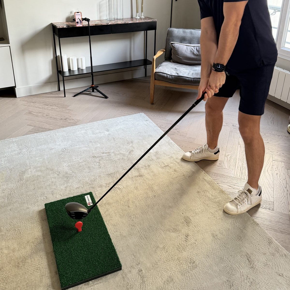 Golfer at address on the mat in a living room, phone on the tripod behind