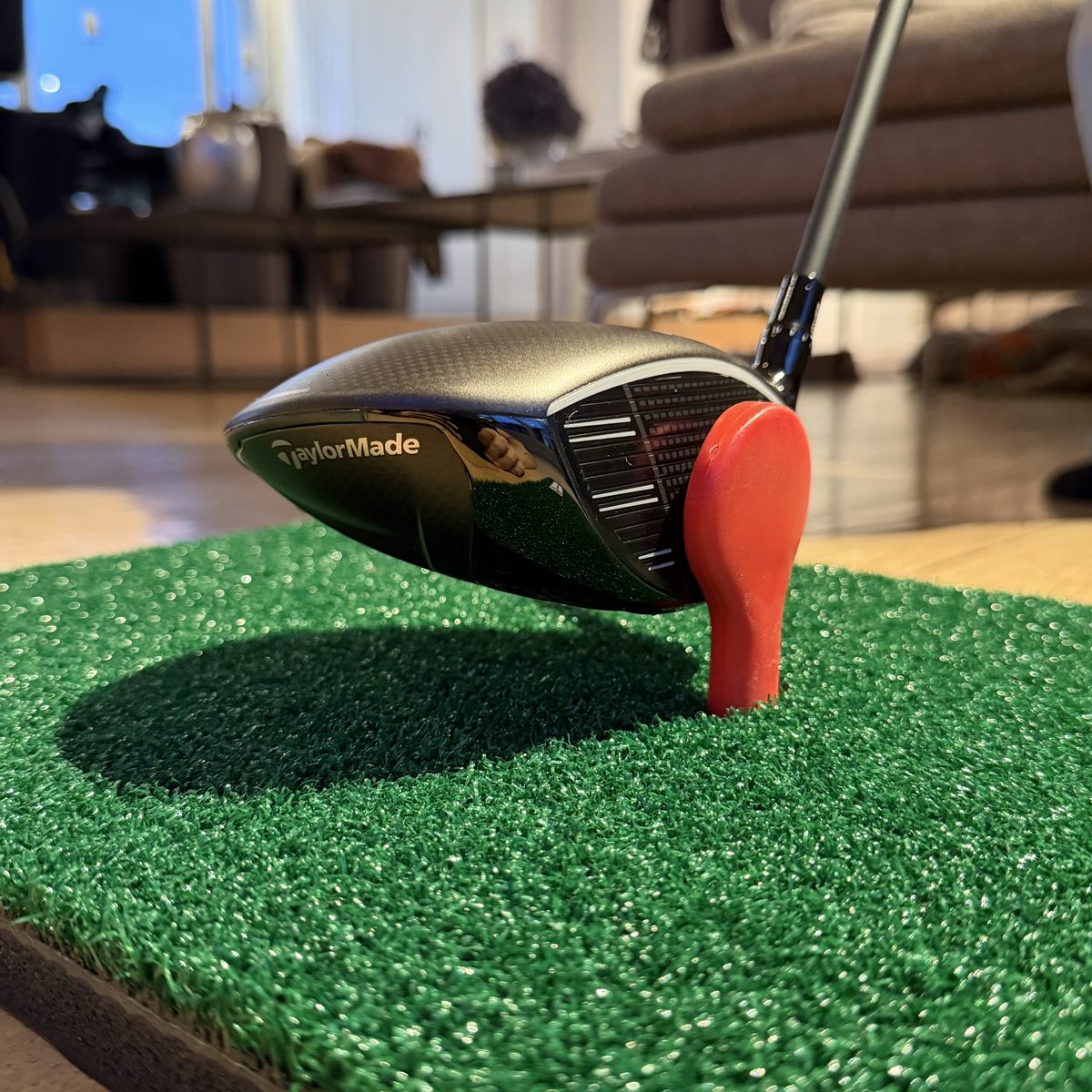 Driver head set up against the red strike target on the mat, side view