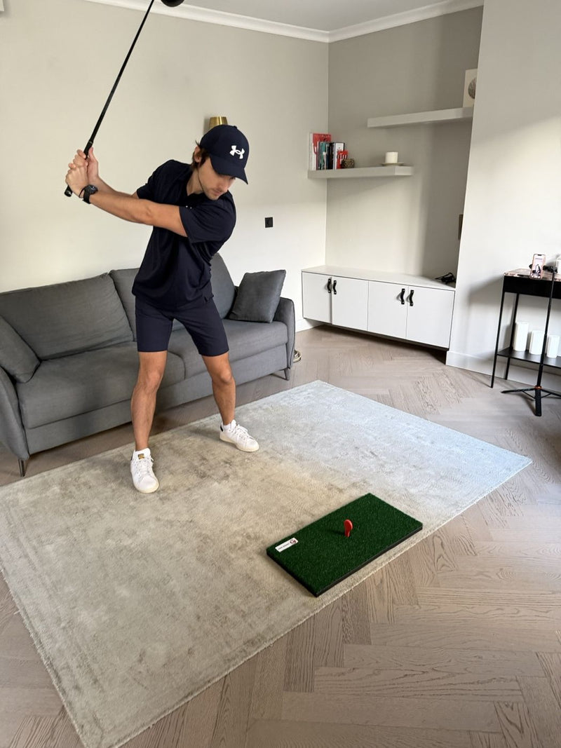 Golfer at the top of his backswing in a living room, the mat on the rug